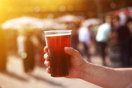 Man holding a jar of dark beer in his hand at the beer and food street festival. Warm sunlight.の写真素材