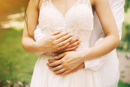 Bride and groom hands close up in the sunny day in the park. Concept of love, wedding and familyの写真素材