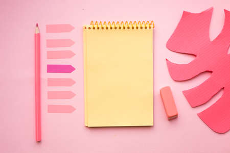 Blank page of vertical spiral note pad with crayon, eraser and artificial monstera leaf on pink background, flat lay. Back to school.の写真素材