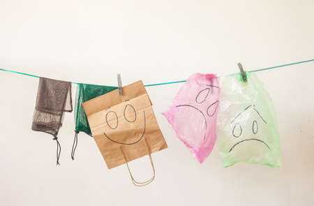 Hanging plastic bags with sad emotions and paper and eco bags with happy emotion against white background. Ecology concept. Plastic issue.の写真素材