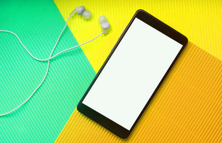 Top view of black smartphone with white headphones on trendy multicolor neo mint vibrant background. Minimal flat lay.の写真素材