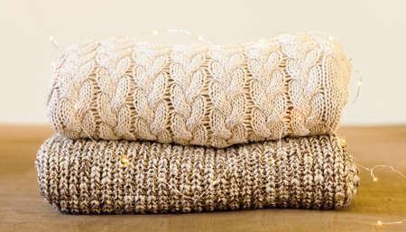 A pile of knitted winter or autumn sweaters on the wood bed decorated with lights. Warm comfortable clothes.の写真素材