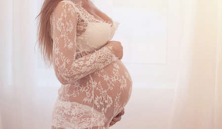 Close up of pregnant belly of young woman against white background. Concept of maternity, pregnancy and child careの写真素材