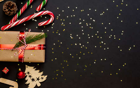 Christmas holiday festive dark black background. Flat lay, top view. Decorations, pine branch and cones, candy and gift box. Golden star shiny confetti.の写真素材