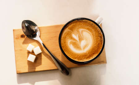 Cup of latte coffee with foam from above, spoon and sugar on white background. Sunny day.の写真素材