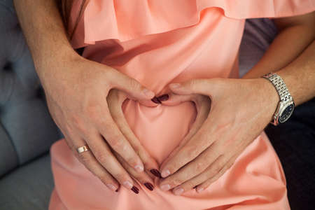 Hands of man and woman on pregnant belly in the shape of heart. Concept of family, child birth, pregnancy.の写真素材