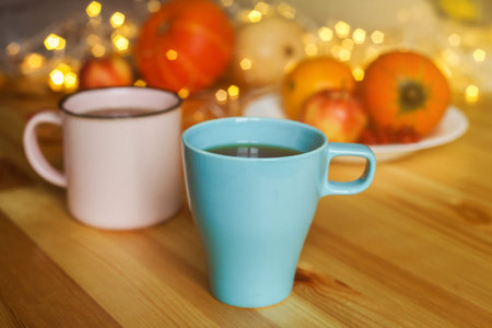 Two cups of tea on wood table against blurred lights, pumpkins, apples and autumn decorations on the window. Autumn, home decor concept.の写真素材