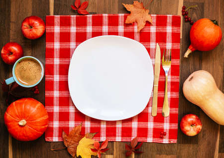 Empty white plate for text, red tablecloth, pumpkins and apples against wood dark background. Autumn or fall holiday festive concept.の写真素材