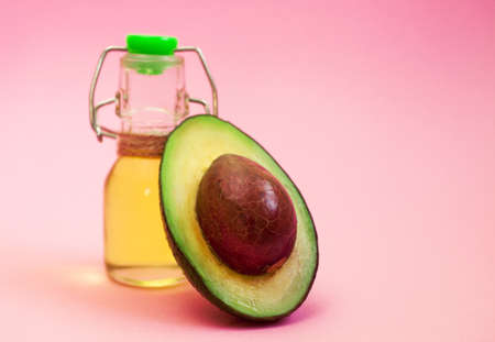 Avocado and avocado oil in bottle on pink background. Top view. Copy space. Beauty product for skin care, wellness and medical purposes.の写真素材