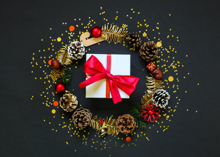 Chirstmas wreath decoration and gift box. Flat lay, top view. Black background. Golden confetti....