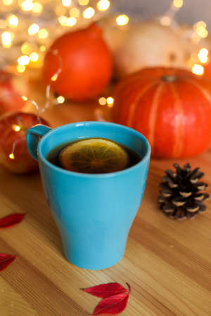 Cup of tea on wood table against blurred lights, pumpkins, apples and autumn decorations on the window. Autumn, home decor concept.の写真素材