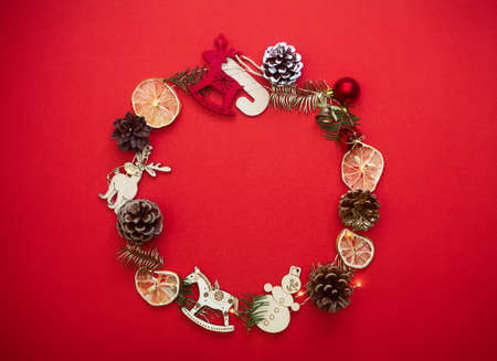 Chirstmas wreath decoration with pine cones, balls and toys. Flat lay, top view. Red background. Copy space.の写真素材