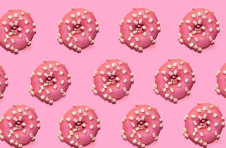 Pattern of trendy pink frosted donut with white marshmallows on pink background. Top view, flat lay, copy space. Unhealthy fast junk food concept.の写真素材