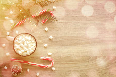 Christmas flat lay with pink cup of coffee with marshmallows and candies on wooden background. Sparkling lights bokeh effect.の写真素材