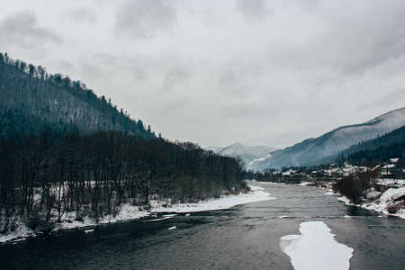 Winter scenery of river in the mountains and forest. Cloudy grey sky. Beautiful winter overcast landscape.の写真素材
