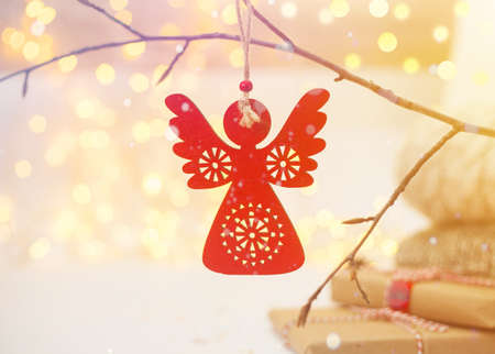 Red Christmas angel toy and gift boxes. Blurred lights shiny golden bokeh backgound. New Year and winter holidays concept. Warm knitted sweaters. Snow effect.の写真素材