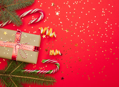 Christmas greeting card with a space for text, flat lay, top view, copy space. Red background with golden star confetti. Branches, orange peelの写真素材