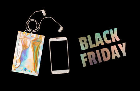 Black Friday shopping sale concept with phone, bag and earphones on black background. Iridescent holographic textの写真素材