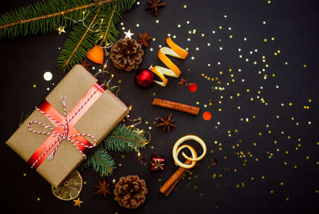 Christmas greeting card with a space for text, flat lay, top view, copy space. Black background with golden star confetti. Branches, orange peel, gift box.の写真素材