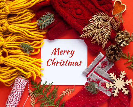 Merry Christmas card. Winter socks, knitted scarf and gloves. Tree branches and candies. Red background. Flat lay, top view. Seasonal warm clothes.の写真素材
