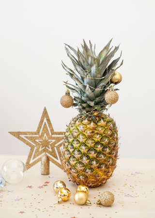 Pineapple decorated wih Christmas golden balls on white background, holiday Christmas or new year concept of decor. Exotic summer festive picture. Zero waste.の写真素材