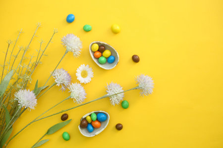 Chocolate Easter Eggs with colorful candies over yellow background, flowers and copy space for text