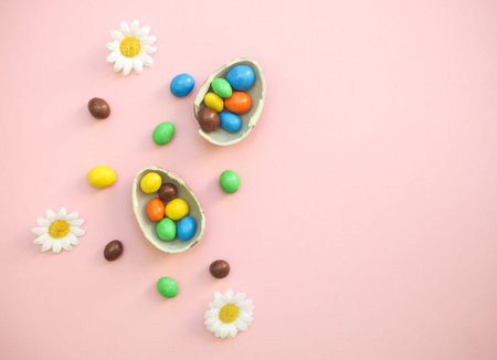 Chocolate Easter Eggs with colorful candies over pink background, flowers and copy space for textの写真素材