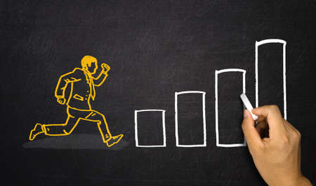 businessman jumping over charts on blackboardの写真素材