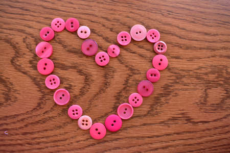 pink sewing buttons in the shape of a heart on woodの写真素材