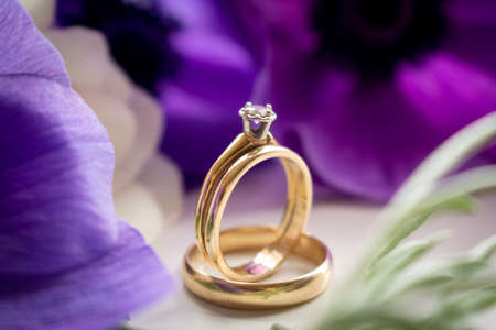 wedding rings and purple flowers on a white background with greeneryの写真素材