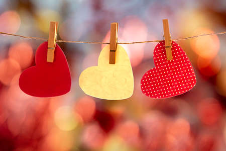 red hearts hanging on a string with a red bokeh backgroundの写真素材
