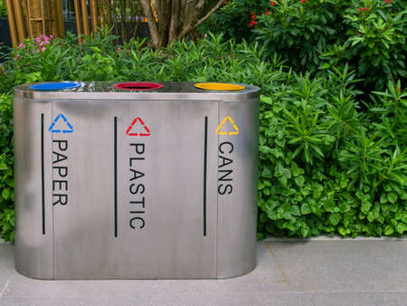 recycle waste management trash separate by can bin yellow color plastic bin red color and paper bin blue color made by stainless steel front of green leaves tree shrub in public park for environment conservationの写真素材