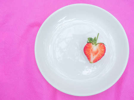 single red heart the strawberry sweet fruit a closeup texture of red berry heart-shaped fruits by half cut in white plate on pink fabric background for juice and dessert or valentine themeの写真素材