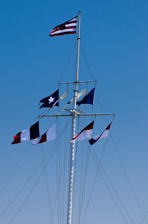 Flags flying on a boat mast with blue sky