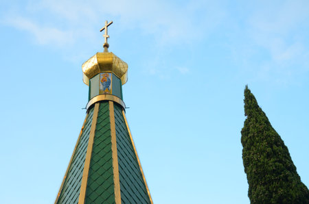 Christian church, cypress tree and pale blue sky. Cone and dome with the golden Christian cross of...