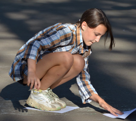 VORONEZH REGION / RF - JULY 2021: kids in a country camp. Funny sport contest: walking on paper sheets. A brown-haired mid-grade girl in a plaid shirt touches (moves) a paper sheet to step on it laterのeditorial素材