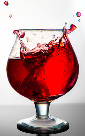 A glass with a red drink explodes with splashes on a gray background