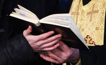The religious book Trebnik is held by the hands of a man and a young man against the background of a priest's cassockの写真素材
