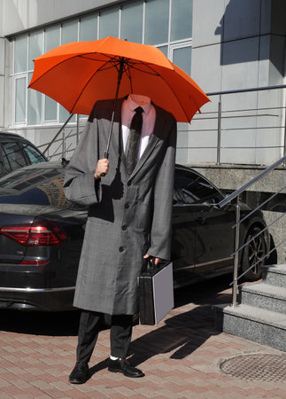 A headless man standing in a raincoat with an umbrella and a suitcaseの写真素材