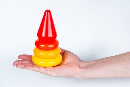 Construction of a colored children's pyramid on a white background. A woman's hand holds a ready-made structure in the palm of her hand. Easy, simple and fast solution of a complex problem. Copy spaceの写真素材