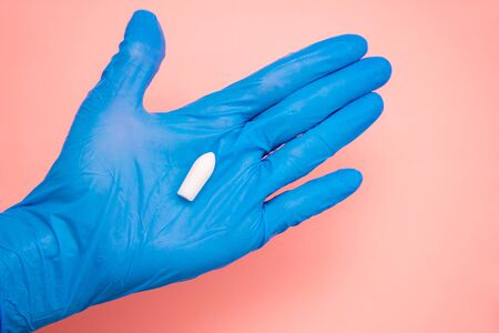 White suppository for anal or vaginal use in hand of a doctor wearing gloves on a pink background. Medical candles for treatment of Candida, thrush, hemorrhoids, inflammation and fever. Copy spaceの写真素材