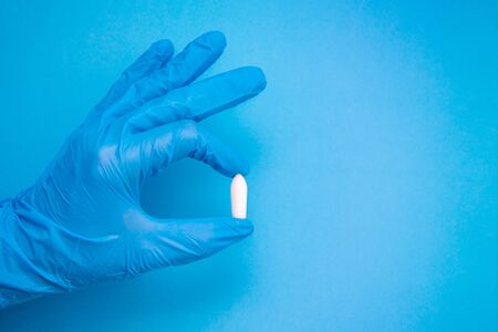 White suppository for anal or vaginal use in hand of a doctor wearing gloves on a blue background. Medical candles for treatment of Candida, thrush, hemorrhoids, inflammation and fever. Copy spaceの写真素材