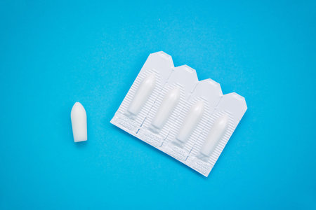 White suppositories for anal or vaginal use on blue background. Medical candles for treatment of...