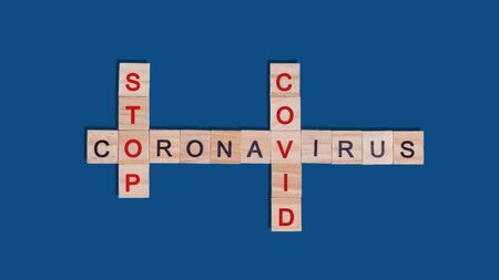 Text crossword puzzle of wooden red and black letters stop coronavirus covid on a blue classic background. Concept of ending quarantine, protection from spread of viral infection during a pandemic.の写真素材