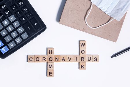 Text from wooden letters coronavirus work from home. Office supplies, a calculator, paper Notepad for notes, a pencil and a protective medical mask on desktop. Flatley layout on a white backgroundの写真素材