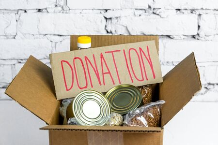 Food in cardboard donation box on a white background. Anti-crisis stock of essential goods for period of quarantine isolation.の写真素材