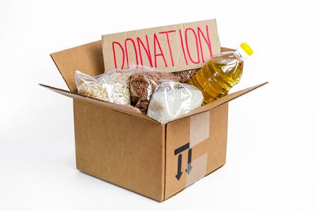 Food in cardboard donation box, isolated on white background. Anti-crisis stock of essential goods for period of quarantine isolation. Food delivery, coronavirus. The shortage of food. Sign with text.の写真素材