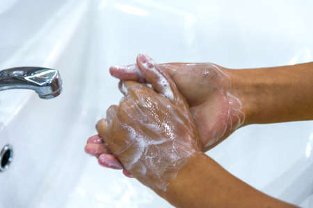A teenage girl washes her hands in soap suds under a stream of water in sink. Clean hands to prevent the spread of bacteria and viral infection. Protection during a pandemic. Hygiene and cleanliness.の写真素材