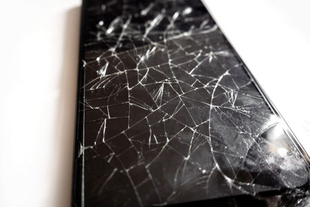 A modern mobile black touch smartphone with a broken glass screen isolated on a white background....