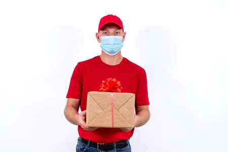 A courier in red uniform and protective medical mask holds box with a bow.の写真素材